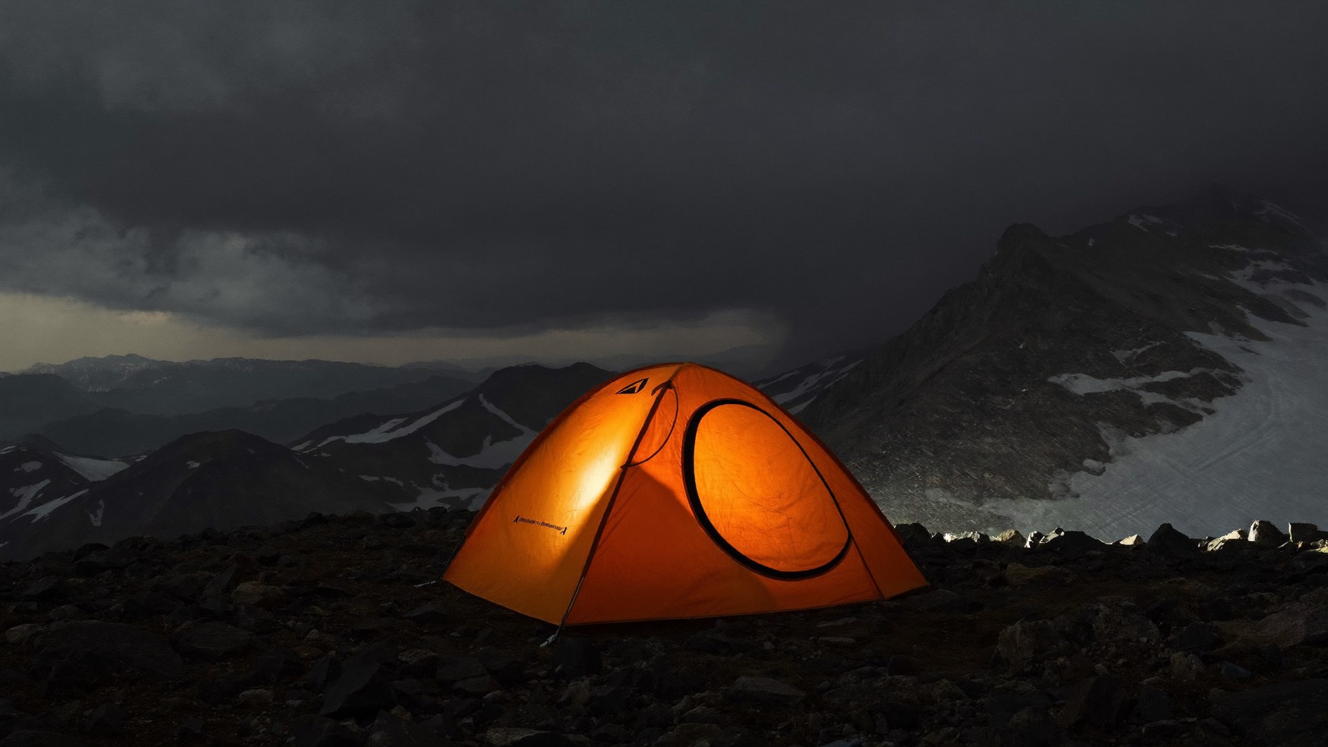 A storm-lit expedition tent pitched on an exposed alpine ridge at dusk, snow driving across the frame.
