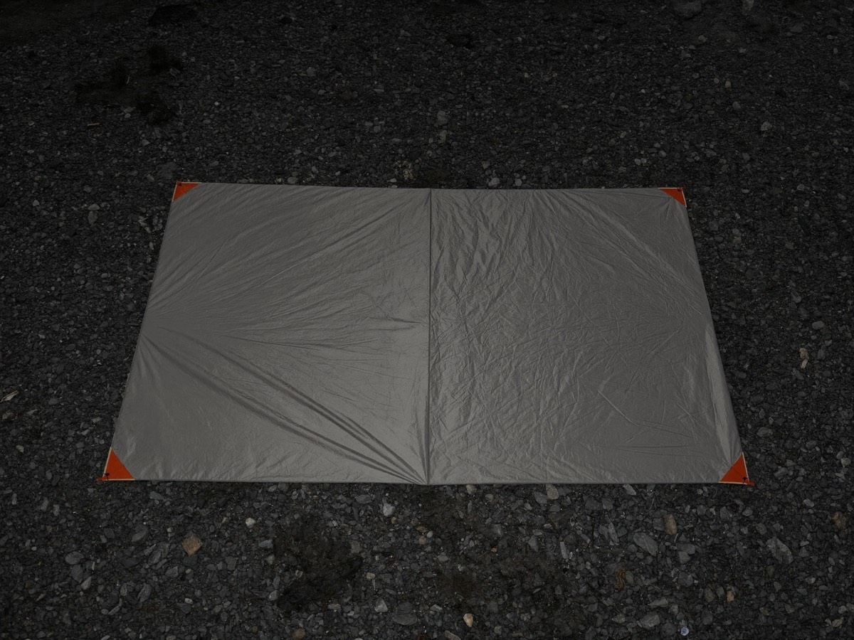Hands smoothing a groundsheet footprint over cleared terrain.