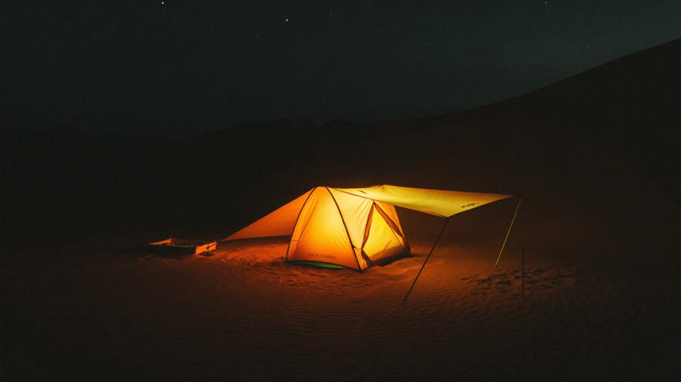 A shade-awning shelter on cracked desert hardpan, heat haze rising off the ground.