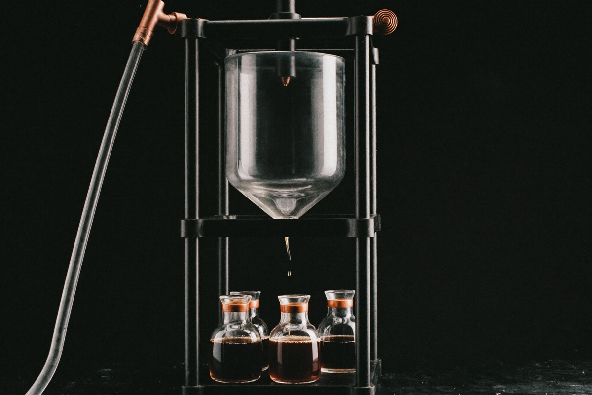 A tall glass carafe of cold brew steeping, coarse grounds suspended in cold water.