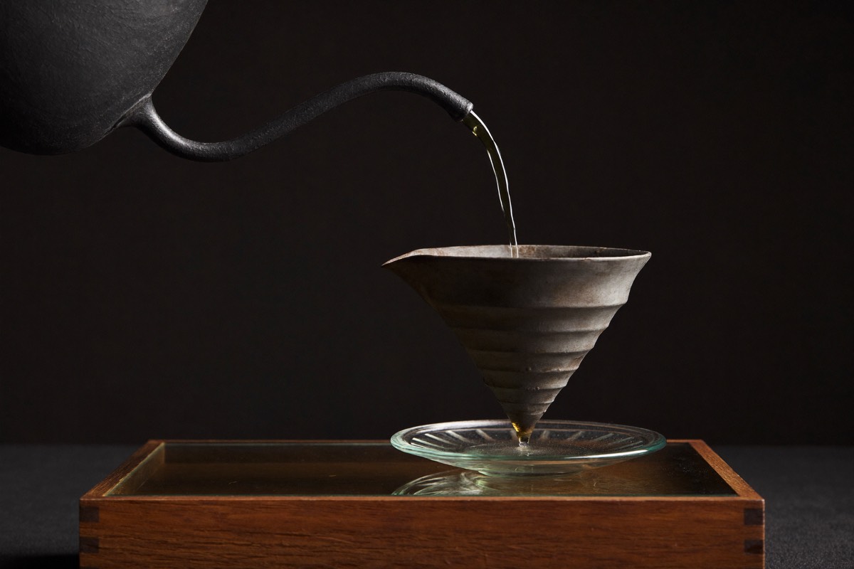 A gooseneck kettle pouring a slow spiral over a paper-filtered pour-over cone.